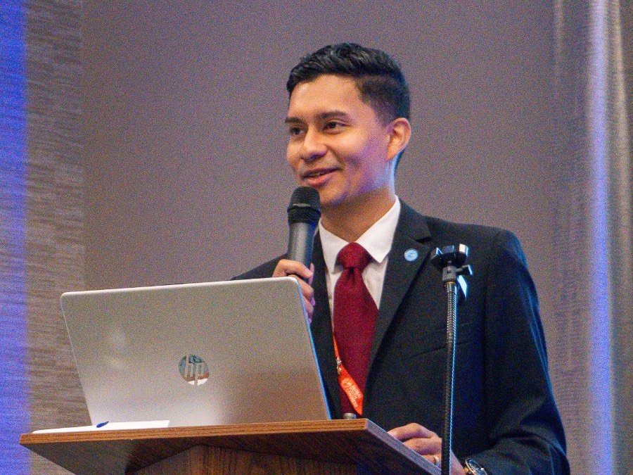 Mau speaking at a podium with a microphone